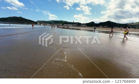 Enthusiastic Beach Walkers Relishing in the Joys of a Beautiful Sunny Day by the Calm Shoreline Enthusiastic Beach Walkers Relishing in the Joys of a Beautiful Sunny Day by the Calm Shoreline 125766600