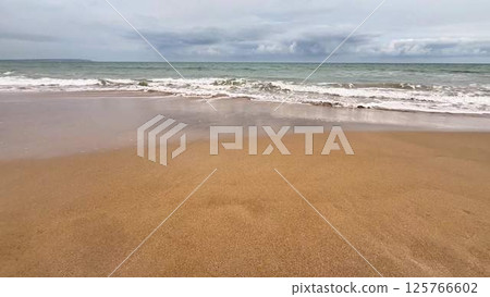 A Serene Beach Landscape Featuring Gentle Waves Lapping Against a Cloudy Sky Above 125766602