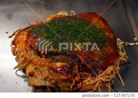 Osaka's specialty okonomiyaki being cooked on a hot plate 125767150
