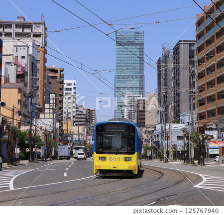 Hankai Electric Tramway - A train running at Matsumushi Station with the Harukas in the background Hankai Electric Tramway - A train running at Matsumushi Station with the Harukas in the background 125767940