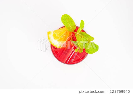 vibrant red berry cocktail with orange slice and fresh mint leaves served in clear glass with ice on white background. High quality photo 125769940