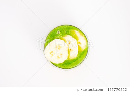green smoothie with banana slices served in clear glass on white background healthy detox drink with tropical fruit topping. High quality photo green smoothie with banana slices served in clear glass on white background healthy detox drink with tropical fruit topping. High quality photo 125770222
