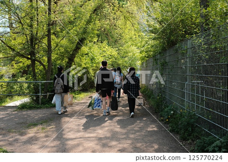 people walking outdoors through sunny park or open paved space during spring with trees and bright sky. High quality photo people walking outdoors through sunny park or open paved space during spring with trees and bright sky. High quality photo 125770224