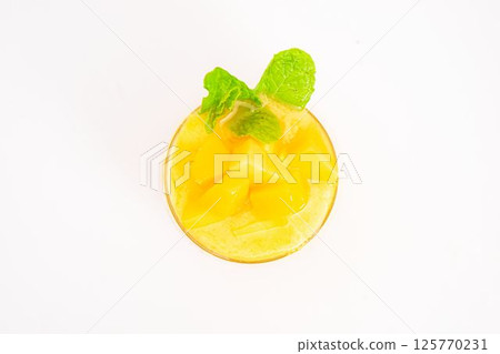 mango or peach smoothie with ice or fruit cubes served in transparent glass and topped with fresh mint leaves on white background. High quality photo 125770231