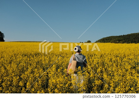 woman in white summer dress and straw hat walking through yellow rapeseed flower field under clear blue sky in countryside. High quality photo woman in white summer dress and straw hat walking through yellow rapeseed flower field under clear blue sky in countryside. High quality photo 125770306