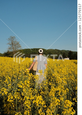woman in white summer dress and straw hat walking through yellow rapeseed flower field under clear blue sky in countryside. High quality photo woman in white summer dress and straw hat walking through yellow rapeseed flower field under clear blue sky in countryside. High quality photo 125770317