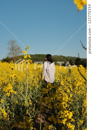 woman in white summer dress and straw hat walking through yellow rapeseed flower field under clear blue sky in countryside. High quality photo woman in white summer dress and straw hat walking through yellow rapeseed flower field under clear blue sky in countryside. High quality photo 125770354