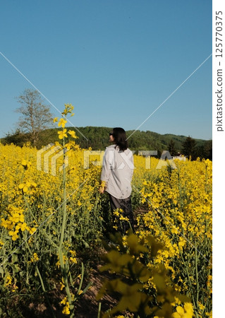 woman in white summer dress and straw hat walking through yellow rapeseed flower field under clear blue sky in countryside. High quality photo woman in white summer dress and straw hat walking through yellow rapeseed flower field under clear blue sky in countryside. High quality photo 125770375