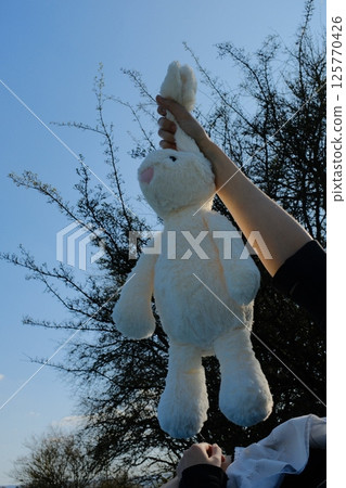 cute white plush rabbit toy held in hand against blue sky background in spring outdoor environment. High quality photo 125770426