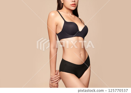 Confident beautiful young asian woman posing in black lingerie on beige background, Perfect body, 125770537