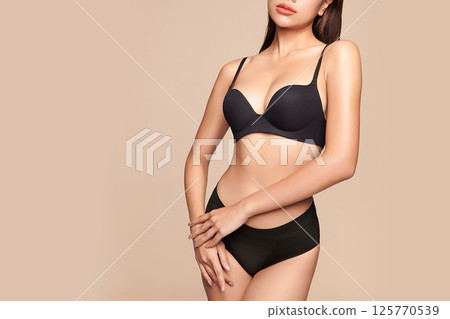 Confident beautiful young asian woman posing in black lingerie on beige background, Perfect body, 125770539