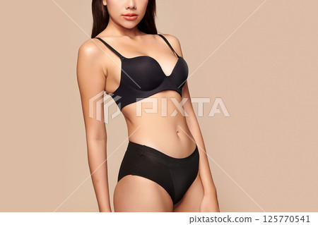 Confident beautiful young asian woman posing in black lingerie on beige background, Perfect body, 125770541