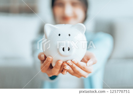 Young Asian woman holding piggy bank and sitting on the floor at home Young Asian woman holding piggy bank and sitting on the floor at home 125770751