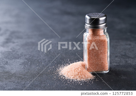 salt shaker with crystals of pink himalayan salt on a black stone table, selective focus. salt shaker with crystals of pink himalayan salt on a black stone table, selective focus. 125772853