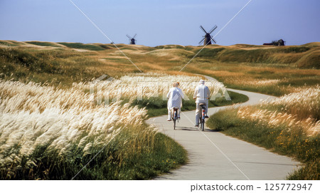 Trail ride on eco route, elderly couple ride on ramp through blooming summer grass to old windmills, eco design of landscape park, meditative tone create visual story for calmness and restoration Trail ride on eco route, elderly couple ride on ramp through blooming summer grass to old windmills, eco design of landscape park, meditative tone create visual story for calmness and restoration 125772947