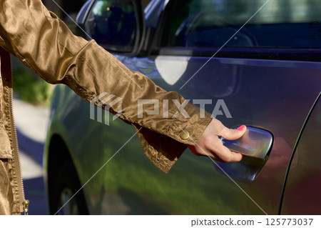 A woman's hand in the sleeve of a brown jacket opens the car door A woman's hand in the sleeve of a brown jacket opens the car door 125773037