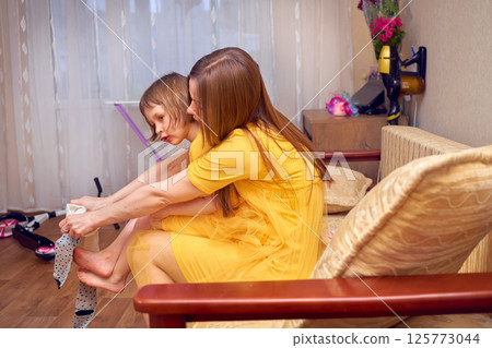 Mom puts on daughter's socks.Getting ready for holiday in yellow clothes Mom puts on daughter's socks.Getting ready for holiday in yellow clothes 125773044