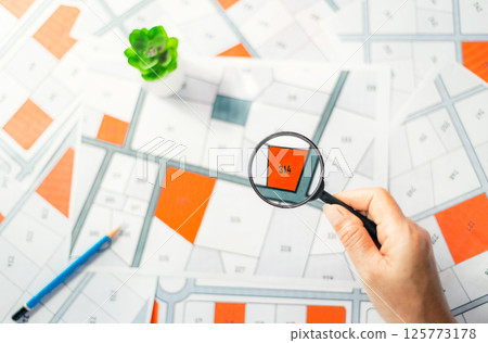 Man holding magnifier on cadastre map search for assesses to buy the land lands. real estate concept with vacant land for building construction and housing subdivision for sale, rent, buy, investment. 125773178
