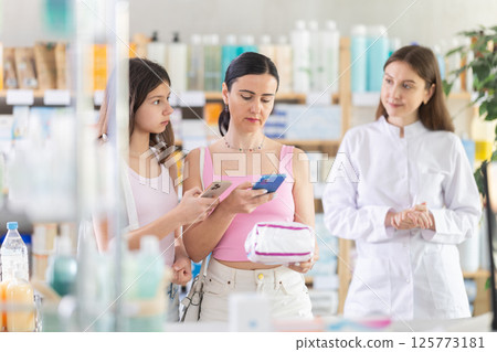 Woman with daughter scans feminine pads qr code with pharmacist 125773181
