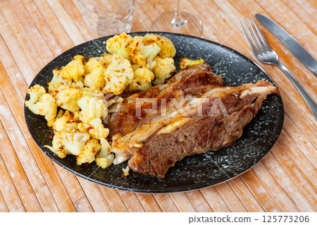 Lunch for restaurant guest - fried fatty and juicy lamb and vegetable side dish of cauliflower 125773206