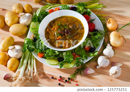 Tasty goulash from chicken hearts with lettuce at plate, fresh vegetables 125773251