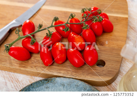 Branch of red cherry plum tomatoes lying on wooden cutting board Branch of red cherry plum tomatoes lying on wooden cutting board 125773352