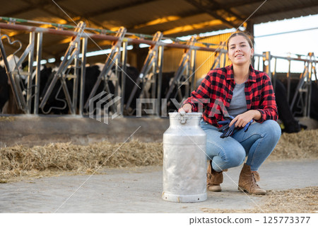 Cheerful girl posing with milk can in cowshed on dairy farm Cheerful girl posing with milk can in cowshed on dairy farm 125773377