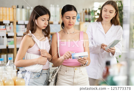 Woman with daughter choosing ointment with pharmacist Woman with daughter choosing ointment with pharmacist 125773378