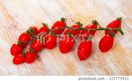 Banch of ripe red cherry plum tomatoes lying on wooden surface Banch of ripe red cherry plum tomatoes lying on wooden surface 125773411