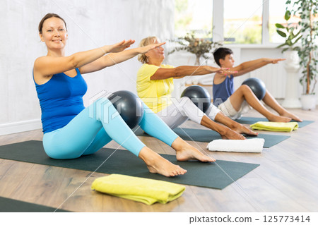 Family grandmother, mother and grandson perform fitness exercise sitting on floor with softball 125773414