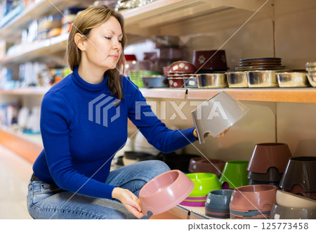 Young woman choosing bowl for puppy in pet supplies store 125773458