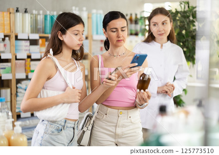 Woman with daughter scans syrup qr code with pharmacist Woman with daughter scans syrup qr code with pharmacist 125773510