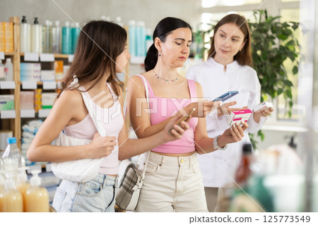 Family of mother and daughter clients choosing box of paracetamol antipyretic pills, scan QR code on label, looking at composition of medicine in drug store, young professional woman pharmacist 125773549
