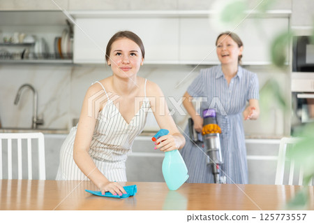 Young girl cleaning the table surface, mother vacuum-cleaning in the kitchen Young girl cleaning the table surface, mother vacuum-cleaning in the kitchen 125773557