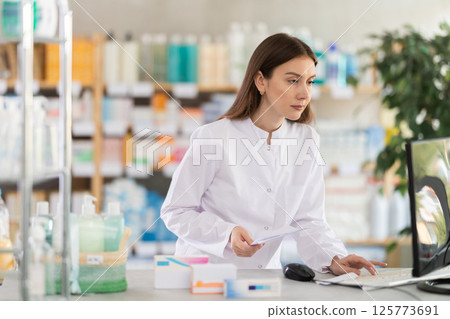 Young female pharmacist working with computer in chemist's shop Young female pharmacist working with computer in chemist's shop 125773691