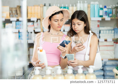 Woman and girl daughter in pharmacy scans QR code on sun protection cream Woman and girl daughter in pharmacy scans QR code on sun protection cream 125773711
