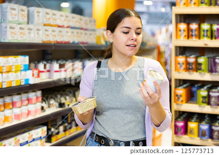 Young happy woman choosing canned pet food in pet shop Young happy woman choosing canned pet food in pet shop 125773713