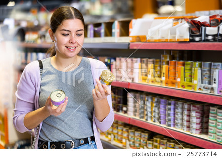 Young woman choosing canned wet food for cat in pet store Young woman choosing canned wet food for cat in pet store 125773714