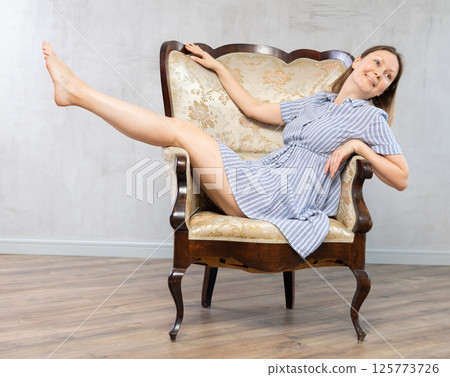 Girl settled down in vintage armchair with legs raised on armrest , put feet on handle of furniture 125773726