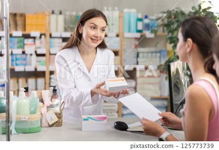 Portrait of woman pharmacist standing at prescription counter and helping mother and daughter choosing pill box and making decisions about pharmaceuticals and health care at pharmacy shop 125773739