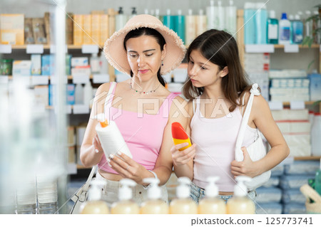 Portrait of interested mother and daughter customers holding and selecting sunscreen cream or sun protection product in drugstore Portrait of interested mother and daughter customers holding and selecting sunscreen cream or sun protection product in drugstore 125773741