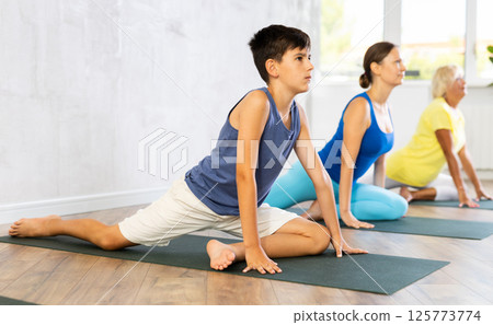 Mother, grandmother and teen son do exercise dove pose, Eka Pada Rajakapotasana. Mother, grandmother and teen son do exercise dove pose, Eka Pada Rajakapotasana. 125773774