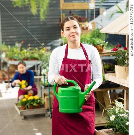 Gardener woman standing near various potted plants holding watering can in container garden 125773788