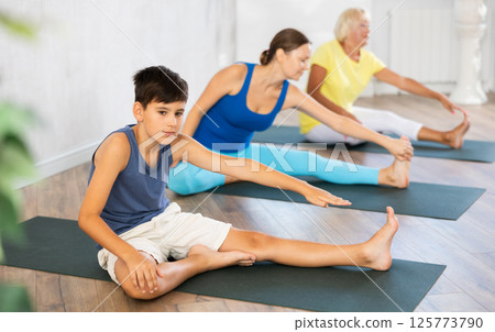 Mother, grandmother and adolescence son do exercise Janu Shirshasana pose. Mother, grandmother and adolescence son do exercise Janu Shirshasana pose. 125773790