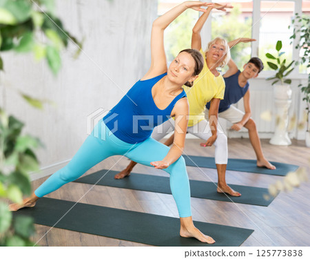 Mom, grandmother and teen grandson performing lateral elongated angle pose Utthita Parshvakonasana 125773838
