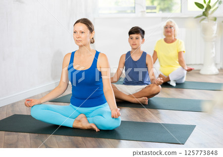 Family three generations do half lotus position Sidhasana with hands clasped in mudra of knowledge 125773848