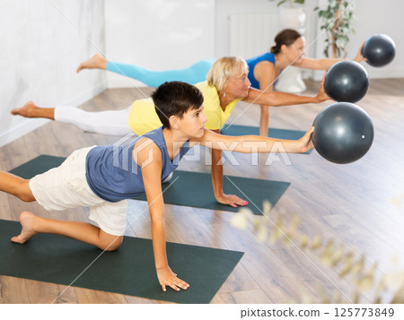 Preteen boy practicing balancing table pose of yoga holding ball in hand 125773849