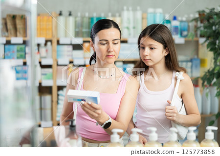 Attentive mother and daughter buyers choosing medical ointment and reading composition of medicine on box in pharmacy 125773858