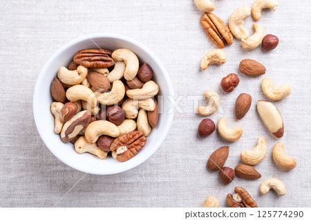 Roasted nuts, crunchy nut mix, quick snack food in a white bowl on linen. Blend of roasted cashews, with almonds, hazelnuts, Brazil nuts, and pecan nuts. Source of protein, fiber and unsaturated fats. 125774290