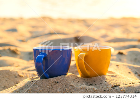 Blue yellow ceramic cups for coffee tea beverages on sunny yellow sand 125774314